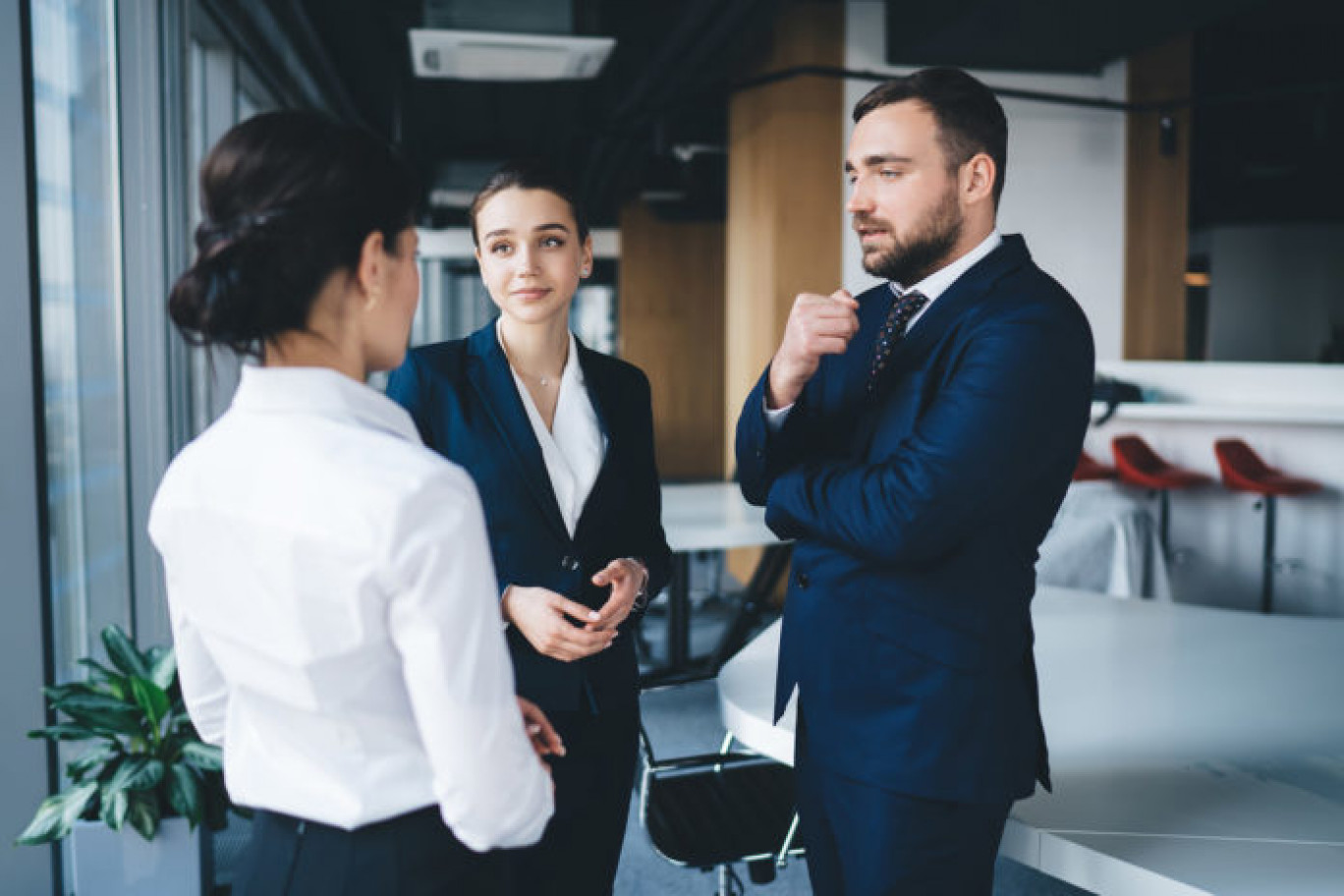 Thoughtful successful coworkers in formal outfit talking and gesturing while standing together beside table at urban conference room in daylight